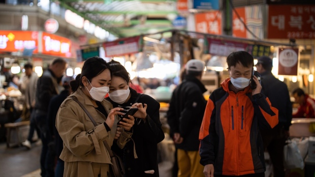 People wearing protective face masks look at a smartphone at Gwangjang Market in Seoul, South Korea, on Friday, April 24, 2020. South Korea reported six more coronavirus cases for the past 24 hours on Friday. New cases have slowed from a daily peak of more than 900 in late February. Photographer: SeongJoon Cho/Bloomberg