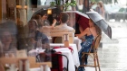 Customers sitting outside at a restaurant in New York hold up umbrellas while it rains on July 11. Photographer: Alexi Rosenfeld/Getty Images