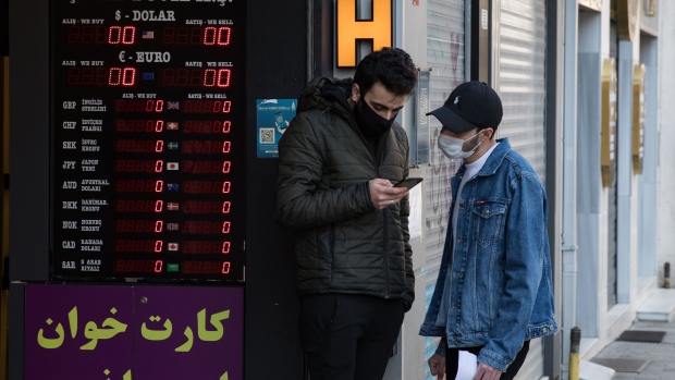 Customers wearing protective face masks check a smartphone outside an electronic currency exchange rate board in Istanbul, Turkey, on Monday, April 27, 2020. Coming off a brief recession just over a year ago, the urgency is mounting for Turkey to loosen the screws on the economy as its currency and reserves come under pressure more than a month after it introduced social-distancing measures. Photographer: Kerem Uzel/Bloomberg