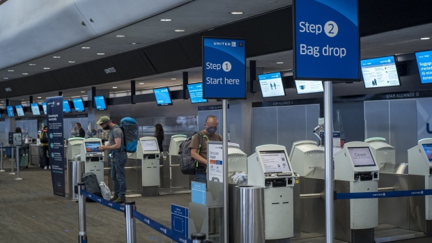 Travelers wearing protective masks use kiosks to check-in at a United Airlines Holdings Inc. counter at San Francisco International Airport (SFO) in San Francisco, California, U.S., on Wednesday, July 1, 2020. United Airlines Holdings Inc. plans to boost its domestic schedule for August to 48% of last years level, from 30% in July, offering another sign of rebounding travel demand. Photographer: David Paul Morris/Bloomberg