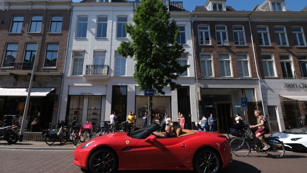 AMSTERDAM, NETHERLANDS - MAY 9: An open roof Ferrari vehicle passes people waiting to enter a Chanel store in P.C. Hoofstraat (Pieter Cornelisz Hooftstraat) luxury fashion shopping street on May 9, 2020 in Amsterdam, Netherlands. (Photo by Yuriko Nakao/Getty Images)
