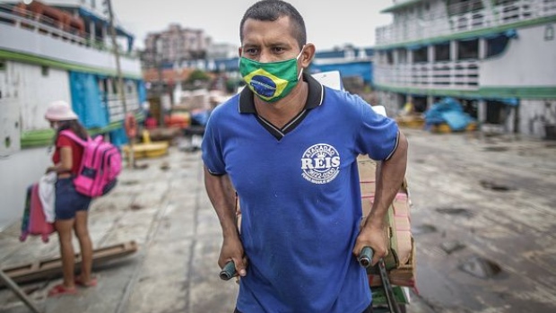 MANAUS, BRAZIL - MAY 19: A man wearing a protective mask with a Brazilian flag carries provisions to boats at Manaus port on May 19, 2020 in Manaus, Brazil. This traditional trade area at the Amazonas riverbanks remains running despite to coronavirus (COVID-19) pandemic. (Photo by Andre Coelho/Getty Images)