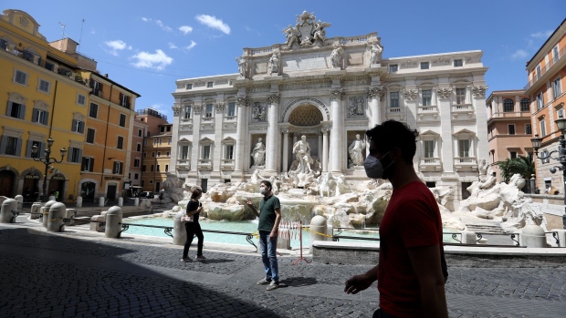 Pedestrians, wearing protective face masks, walk in view of the Trevi Fountain in Rome, Italy, on Tuesday, May 19, 2020. Italy registered the lowest number of new coronavirus cases since early March as the government eased a nationwide lockdown Monday allowing shops, bars and restaurants to reopen as long as they respect health and safety rules. Photographer: Alessia Pierdomenico/Bloomberg