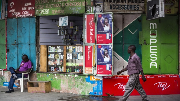 A pedestrian passes in front of a mobile phone accessories and M-Pesa banking service vendor in Mombasa, Kenya, on Thursday, Nov. 23, 2017. The country’s Treasury has already cut this year’s growth target to 5 percent from 5.9 percent as the protracted election furor damped investment and a drought curbed farm output. Photographer: Luis Tato/Bloomberg
