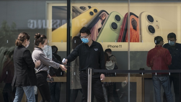 An employee wearing a protective mask checks the temperature of customers outside an Apple Inc. store in Shanghai, China, on Monday, April 20, 2020. Chinese banks lowered borrowing costs and the government promised to sell another 1 trillion yuan ($141.3 billion) in bonds to pay for stimulus spending after the economy had its first contraction in decades due to the coronavirus outbreak.