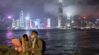 People adjust their hair and a protective mask while posing for a selfie photograph against the city skyline at night in the Tsim Sha Tsui district of Hong Kong, China, on Friday, Feb. 14, 2020. As fears of the novel coronavirus (Covid-19) spread across the region, pharmacies and supermarkets in Hong Kong are running out of basic supplies like toilet paper, paper towels, hand sanitizer and especially masks. Photographer: Justin Chin/Bloomberg