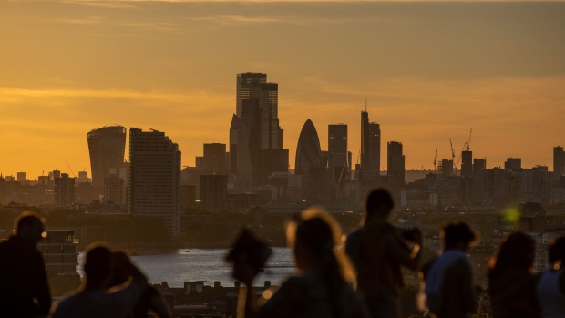 Pedestrians watch the sun set over skyscrapers on the skyline from Greenwich Park in London, U.K., on Thursday, July 30, 2020. London's best offices are forecast to plunge in value by as much as 15% this year as the coronavirus hits rents and investors' appetite for real estate. Photographer: Simon Dawson/Bloomberg