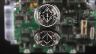 A coin representing Ethereum cryptocurrency sits reflected on a polished surface and photographed against a computer circuit board in this arranged photograph in London, U.K., on Thursday, Feb. 8, 2018. Cryptocurrencies tracked by Coinmarketcap.com have lost more than $500 billion of market value since early January as governments clamped down, credit-card issuers halted purchases and investors grew increasingly concerned that last year’s meteoric rise in digital assets was unjustified.