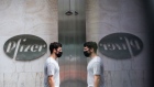 A pedestrian wearing a protective mask passing in front of Pfizer Inc. signage is reflected outside the company's headquarters in New York, U.S., on Wednesday, July 22, 2020. U.S. health officials agreed pay $1.95 billion for 100 million doses of a vaccine made by Pfizer Inc. and BioNTech SE, the latest step in an effort to fight the coronavirus pandemic.