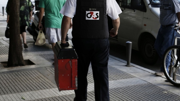 A G4S Plc security guard returns to his van after delivering cash to a bank branch in Thessaloniki, Greece. Photographer: Konstantinos Tsakalidis/Bloomberg