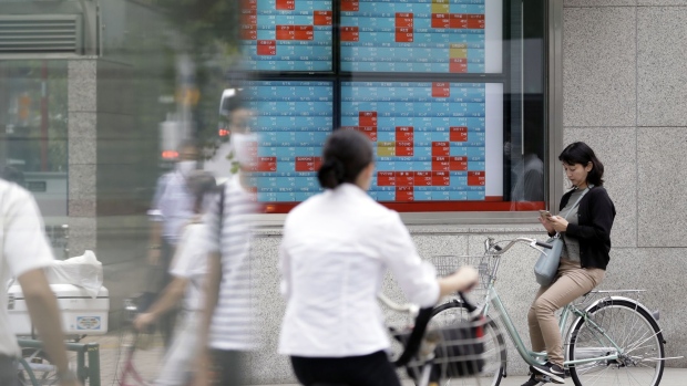 A woman uses a smartphone on her bicycle in front of an electronic stock board outside a securities firm in Tokyo, Japan, on Thursday, Sept. 17, 2020. Japanese stocks were set for their fourth straight weekly gain, the longest winning streak since November, as investors moved back in following this week’s central bank rate decisions at home and in the U.S. Photographer: Kiyoshi Ota/Bloomberg