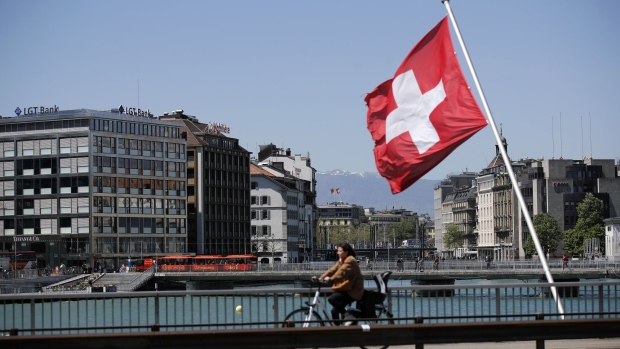 A cyclist passes a Swiss national flag on a bridge in Geneva, Switzerland, on Tuesday, May 14, 2019. While the Swiss city has largely recovered from the end of secrecy at financial institutions, which shrank the number of banks there by a quarter since 2005, it faces questions about its allure for international businesses and the world’s wealthy.