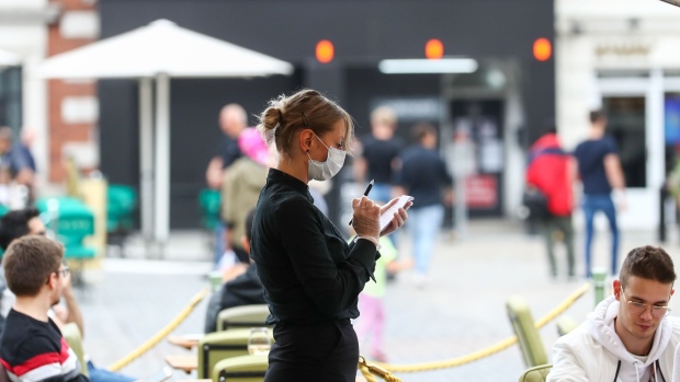 A waitress wearing a protective face mask takes a customer's order at a cafe's terrace in the Covent Garden area of London, U.K., on Saturday, July 4, 2020. Restaurants, hotels, cinemas and hairdressers will also be allowed to open their doors again on what has been dubbed 'Super Saturday' after 3 1/2 months of an economic lockdown brought in to contain the outbreak. Photographer: Simon Dawson/Bloomberg