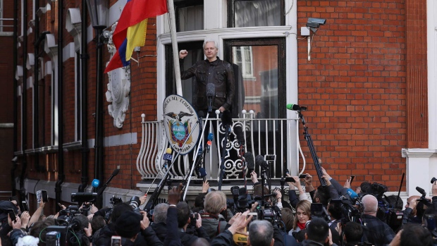 Julian Assange, founder of WikiLeaks, holds up a fist before speaking to media and supporters from a balcony at the Ecuadorian embassy in London, U.K., on on Friday, May 19, 2017. Assange hailed a Swedish decision to drop a rape probe against him, but said he won't leave the Ecuadorian embassy in London where he has sought refuge for the past five years as long as he remains a target in the U.S. and U.K.