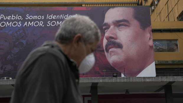 A pedestrian passes by a billboard featuring an image of Nicolas Maduro in Caracas. Photographer: Carlos Becerra/Bloomberg
