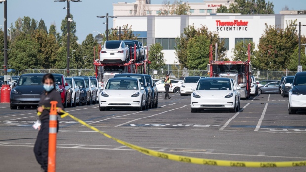 A security guard wearing a protective mask puts up a caution tape at the entrance to the vehicle holding lot outside the Tesla Inc. assembly plant in Fremont, California, U.S., on Tuesday, Sept. 22, 2020.