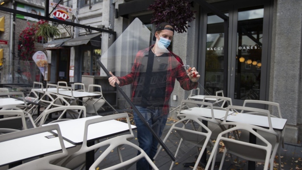 A worker wearing a protective mask carries a plexiglass shield while dismantling a restaurant's terrace in Montreal, Quebec, Canada, on Thursday, Oct. 1, 2020. After a spike in Covid-19 cases, Quebec will force public places including bars, museums, cinemas and restaurant dining rooms to close from Oct. 1 to Oct. 28 in three regions, including greater Montreal and greater Quebec City.