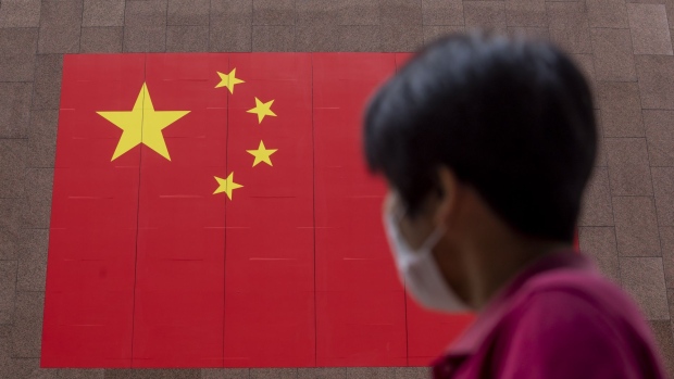 A pedestrian wearing a protective mask walks past a Chinese national flag displayed outside a hotel on National Day in Hong Kong, China, on Thursday, Oct. 1, 2020. Hong Kong leader Carrie Lam declared a return of stability, even as authorities deployed thousands of riot police and threats of arrests to deter protesters from returning to the streets in the Asian financial center. Photographer: Paul Yeung/Bloomberg