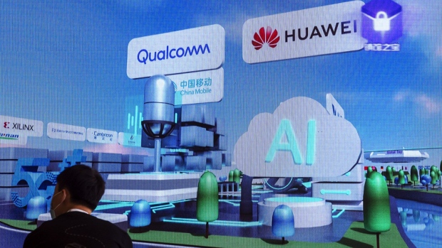 Visitors wearing protective masks sit in front of a screen displaying the logos of Qualcomm Inc. and Huawei Technologies Co. at the World AI Conference in Shanghai, China, on Thursday, July 9, 2020. China will invest an estimated $1.4 trillion over six years to 2025, calling on urban governments and private tech giants to lay fifth generation wireless networks, install cameras and sensors, and develop AI software that will underpin autonomous driving to automated factories and mass surveillance, according to the National People's Congress Work Report released in May.