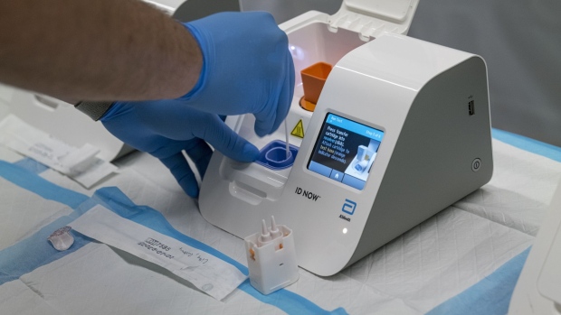 A medical worker wearing personal protective equipment (PPE) uses an Abbott Laboratories ID NOW rapid Covid-19 test machine at San Francisco International Airport (SFO) in San Francisco, California, U.S., on Thursday, Oct. 15, 2020. United and Hawaiian Airlines are offering options for Covid-19 testing to passengers traveling to the state of Hawaii that will include at-home tests, drive-through testing, and in-person tests at the airport.