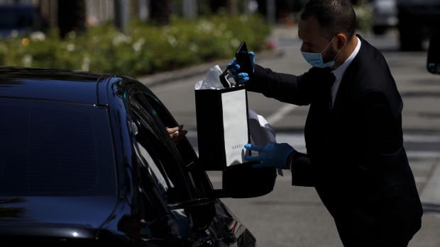 An employee wearing a protective mask and gloves hands a purchase to a customer in a vehicle at a curbside pickup location outside a Gucci Ltd. store on Rodeo Drive in Beverly Hills, California, U.S., on Tuesday, May 19, 2020. The luxury-goods market will shrink between 15% and 35% this year as the coronavirus and efforts to control it hammer sales of high-end goods, consultancy Bain forecast in a report. Photographer: Patrick T. Fallon/Bloomberg