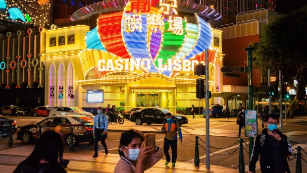 People wearing protective masks walk in front of the Casino Lisboa, operated by SJM Holdings Ltd., at night in Macau, China, on Tuesday, March 3, 2020. Casinos in Macau, the Chinese territory that's the world’s biggest gambling hub, reported a record drop in gaming revenue, as they grappled with the cost of closing down their businesses for 15 days to help contain the deadly coronavirus outbreak. Photographer: Billy H.C. Kwok/Bloomberg