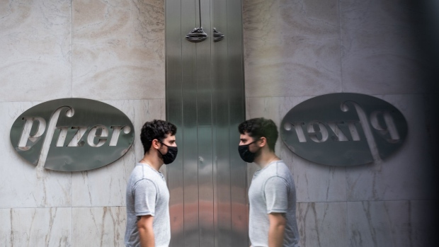 A pedestrian wearing a protective mask passing in front of Pfizer Inc. signage is reflected outside the company's headquarters in New York, U.S., on Wednesday, July 22, 2020. U.S. health officials agreed pay $1.95 billion for 100 million doses of a vaccine made by Pfizer Inc. and BioNTech SE, the latest step in an effort to fight the coronavirus pandemic. Photographer: Jeenah Moon/Bloomberg