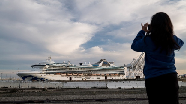 A person takes a photograph of the Carnival Corp. Grand Princess cruise ship docked at the Port of Oakland in Oakland, California, U.S., on Monday, March 9, 2020. The cruise ship that spent days circling the waters off San Francisco with people sickened by the new coronavirus returned to land at an isolated dock, to begin the long process of offloading passengers into quarantine.