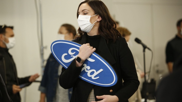 A worker wearing a protective mask holds a Ford sign before a news conference at the Ford Connectivity and Innovation Centre in Ottawa, Ontario, Canada, on Thursday, Oct. 8, 2020. The governments of Canada and Ontario will contribute C$295 million ($223 million) each to Ford Motor Co. to help fund a plan to build electric vehicles in the province, according to a senior government official.