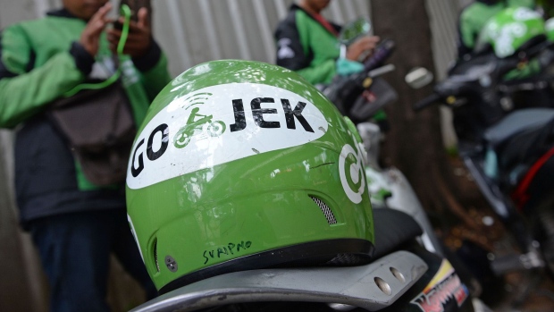 A Go-Jek Indonesia Pt. helmet sits on a motorcycle taxi as riders check their mobile devices in Jakarta. Photographer: Dimas Ardian/Bloomberg