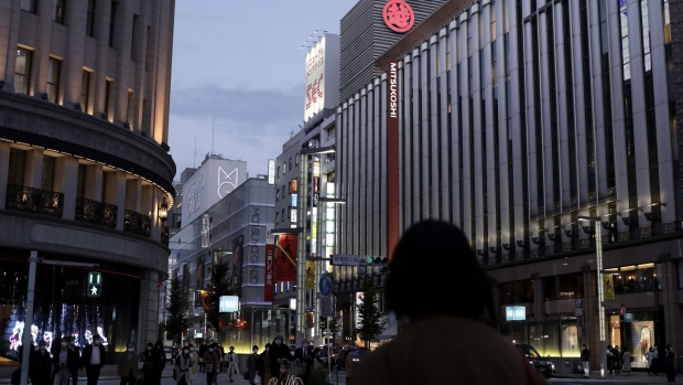 Pedestrians wait to cross a road in front of a Mitsukoshi department store, operated by Isetan Mitsukoshi Holdings Ltd., right, at dusk in the Ginza district of Tokyo, Japan, on Thursday, Nov. 12, 2020. Japan's sharp economic rebound in the last quarter likely recovered only around half the growth lost during the pandemic, official data is expected to show Monday, with weak business investment contributing to slowing momentum going forward.