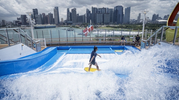 A visitor surfs on the FlowRider surf simulator on the top deck of the The Spectrum of the Seas cruise ship, operated by Royal Caribbean Cruises Ltd.'s cruise line brand Royal Caribbean International (RCI), sits berthed at the Marina Bay Cruise Center in Singapore in 2019.