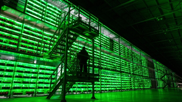An armed guard patrols in front of illuminated mining rigs mounted inside racks at the BitRiver Rus LLC cryptocurrency mining farm in Bratsk, Russia, on Friday, Nov. 8, 2019. Bitriver, the largest data center in the former Soviet Union, was opened just a year ago, but has already won clients from all over the world, including the U.S., Japan and China. Most of them mine bitcoins. Photographer: Andrey Rudakov/Bloomberg