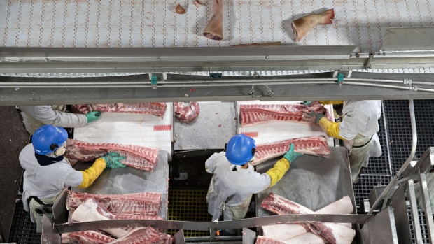 Employees butcher pork ribs as trotters mover along an overhead conveyor at a Smithfield Foods Inc. pork processing facility in Milan, Missouri, U.S., on Wednesday, April 12, 2017. WH Group Ltd. acquired Virginia-based Smithfield, the world's largest pork producer, in 2013 for $6.95 billion. As Smithfield can't export sausage, ham and bacon from its U.S. factories, because China prohibits imports of processed meat, WH Group opened an 800 million-yuan ($116 million) factory in Zhengzhou that will produce 30,000 metric tons of those meats when it reaches full capacity next year. Photographer: Daniel Acker/Bloomberg