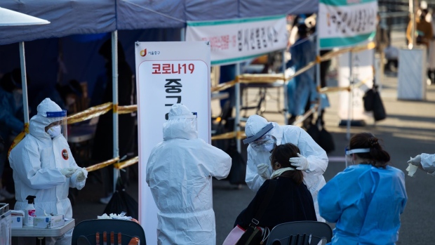 A medical worker wearing personal protective equipment (PPE) collects a sample from a visitor at a temporary Covid-19 testing station outside Seoul Station in Seoul, South Korea, on Monday, Dec. 14, 2020. South Korea reported a drop in new cases on Monday after posting a record of more than 1,000 infections on Sunday and Prime Minister Chung Sye-Kyun said implementing the strictest level of social distancing measures is a last resort.