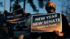 An attendee wears a protective mask while holding a "New Year New Senate" sign during a 'Get Out The Vote' campaign event with U.S. Democratic Senate candidates Raphael Warnock and Jon Ossoff in Garden City, Georgia, U.S., on Sunday, Jan. 3, 2021. Georgia has two runoff elections on Tuesday that will decide control of the U.S. Senate and have a decisive influence on the ability of President-elect Joe Biden to advance his legislative agenda.