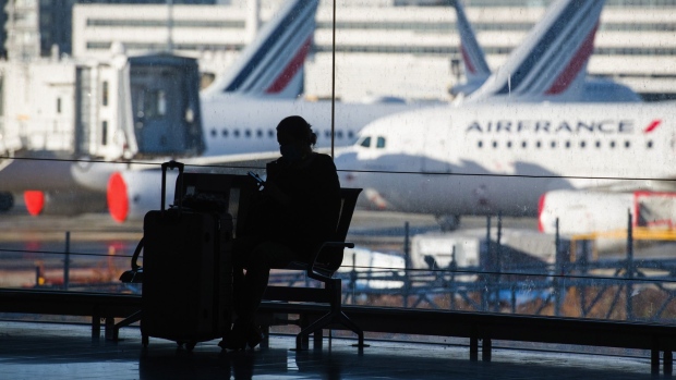 A traveler waits with luggage near passenger aircraft, operated by Air France-KLM, on the tarmac at Charles de Gaulle airport, operated by Aeroports de Paris, in Roissy, France, on Friday, Dec. 18, 2020. The rollout of vaccines against Covid-19 has intensified debate about whether they should be made mandatory, with the head of a major tourism lobby saying that doing so would cause irreparable harm to the struggling sector. Photographer: Nathan Laine/Bloomberg