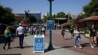 Guests wearing protective masks walk past a face covering sign at Downtown Disney, part of the Disneyland Resort, in Anaheim, California, U.S., on Wednesday, Sept. 30, 2020. Walt Disney Co. is slashing 28,000 workers in its slumping U.S. resort business, marking of one of the deepest workforce reductions of the Covid-19 era. Photographer: Patrick T. Fallon/Bloomberg