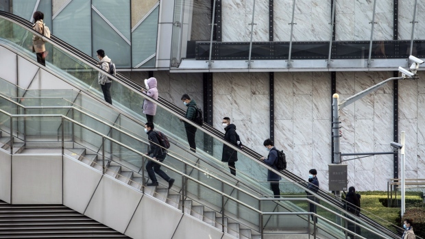 Pedestrians wearing protective masks ride on an escalator in Pudong's Lujiazui Financial District in Shanghai, China, on Thursday, Feb. 18, 2021. China's stock benchmark erased gains after briefly surpassing its 2007 closing peak, as mainland financial markets opened for the first time following the Lunar New Year break. Photographer: Qilai Shen/Bloomberg