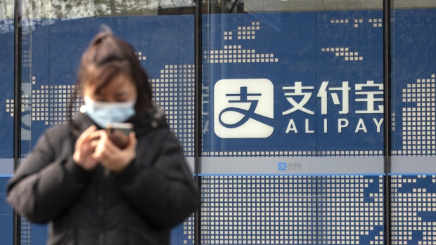 A pedestrian uses a smartphone in front of an Alipay sign outside an Ant Group Co. office building in Shanghai, China, on Thursday, Dec. 24, 2020. China kicked off an investigation into alleged monopolistic practices at Alibaba Group Holding Ltd. and summoned affiliate Ant Group to a high-level meeting over financial regulations, escalating scrutiny over the twin pillars of billionaire Jack Ma’s internet empire. Photographer: Qilai Shen/Bloomberg