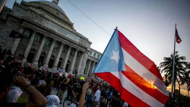 A demonstrator waves a Puerto Rican flag outside the Capitol building during a protest against the government in San Juan, Puerto Rico, on Monday, Jan. 20, 2020. People in a southern Puerto Rico city discovered a warehouse filled with unused emergency supplies, then set off a social media uproar Saturday when they broke in to retrieve goods as the area struggles to recover from a strong earthquake, the Associated Press reported. Photographer: Xavier Garcia/Bloomberg