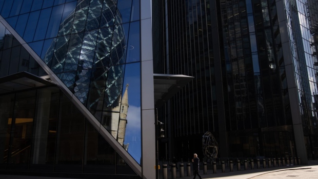 A pedestrian passes office buildings reflecting One St. Mary's Axe, also known The Gherkin, in London, U.K., on Monday, March 22, 2021. U.K. Prime Minister Boris Johnson told the country that people 'must' stay at home and certain businesses must close on March 23, 2020. Photographer: Jason Alden/Bloomberg