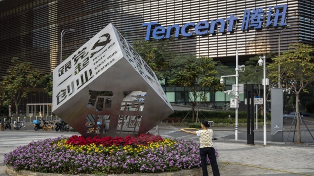 A worker waters the flowers around an installation reading "Follow Our Party Start Your Business" in front of the Tencent Holdings Ltd. headquarters in Shenzhen, China, on Saturday, March 20, 2021.