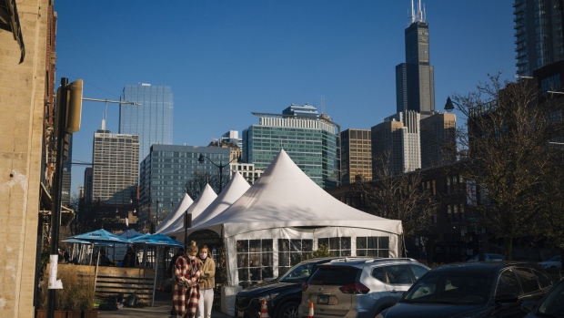 Pedestrians wearing protective masks walk past outdoor dining tents in Chicago, Illinois, U.S., on Friday, Nov. 13, 2020. Stay-at-home advisories took effect in Chicago and suburban Cook County early Monday, with officials urging residents to only leave home for essential activities in an effort to curb the spread of the deadly coronavirus, reported NBC Chicago. Photographer: Taylor Glascock/Bloomberg
