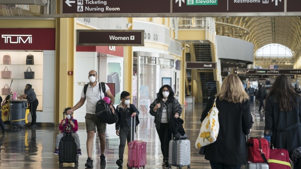 A family wear protective face masks while carrying luggage at the Ronald Reagan National Airport (DCA) in Arlington, Virginia, U.S., on Monday, March 16, 2020. The airline industry, ravaged by plummeting bookings due to the coronavirus, is seeking grants and loans totaling as much as $58 billion from the U.S. government as well as temporary relief from various taxes. Photographer: Sarah Silbiger/Bloomberg