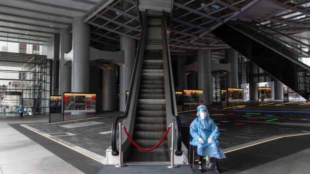 A security guard wearing personal protective equipment (PPE) sits next to an escalator at the HSBC Holdings Plc headquarters building, temporary closed due to the coronavirus, in Hong Kong, China, on Wednesday, March 17, 2021. HSBC's main Hong Kong office was closed until further notice after three people working in the building tested positive for Covid-19 amid a renewed wave of infections among the city’s business and expatriate community.