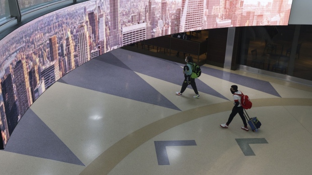 Travelers wearing protective masks walk through Terminal 4 at John F. Kennedy International Airport in New York.