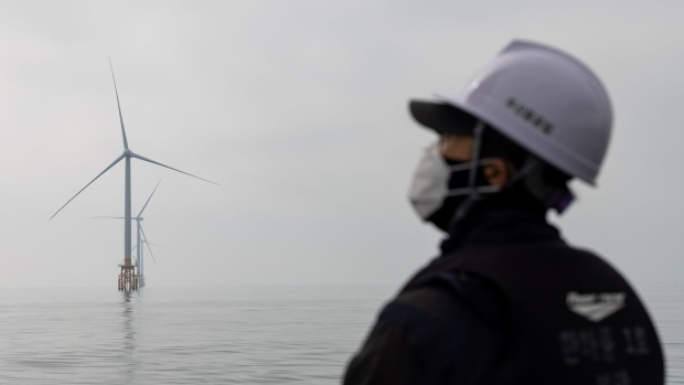 A worker wearing a protective mask stands on a boat as wind turbines operate at Southwest Offshore Wind Farm in Buan, South Korea, on Thursday, March 25, 2021. The wind farm complex in the Southwest Sea will be expanded to 2.46 GW after 2027, according to Korea Offshore Wind Power Corp, a special purpose company formed by state-run Korea Electric Power Corp. and six other generators. Photographer: SeongJoon Cho/Bloomberg