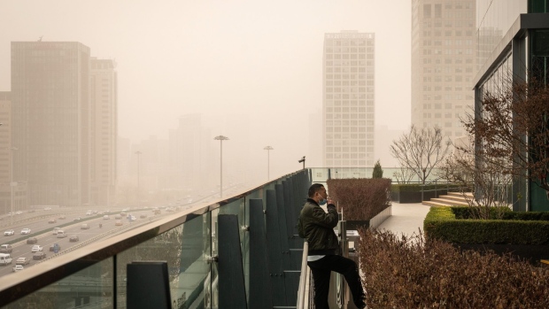 A person smokes a cigarette on a balcony as buildings in the background are shrouded in polluted air in Beijing, China, on Monday, March 15, 2021. A sandstorm sweeping across much of northern China left the city in an orange fog and helped push air quality levels in the capital to the worst since 2017. Photographer: Yan Cong/Bloomberg