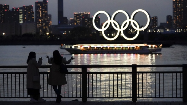 People watch illuminated Olympic rings floating in the waters off Odaiba island in Tokyo, Japan, on Thursday, April 1, 2021. The Tokyo Olympic Games organizers said on March 20 that spectators from overseas wouldn’t be allowed so as to limit crowd size. It’s still unclear how many local fans might be permitted to enter stadiums.